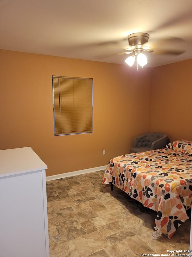 bedroom featuring stone finish flooring, a ceiling fan, and baseboards