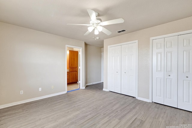 unfurnished bedroom featuring multiple closets, visible vents, light wood-style flooring, and baseboards