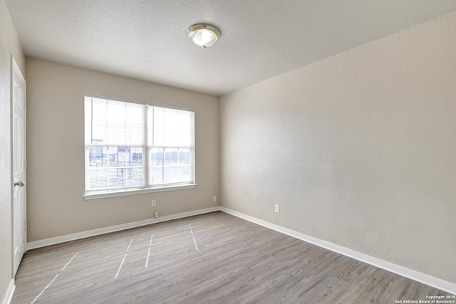 empty room featuring light wood-type flooring, baseboards, a textured ceiling, and a textured wall