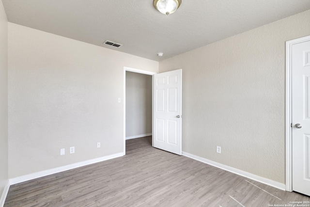 unfurnished bedroom featuring baseboards, a textured ceiling, visible vents, and wood finished floors