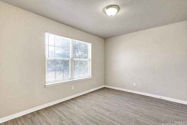 spare room featuring a textured ceiling, wood finished floors, and baseboards