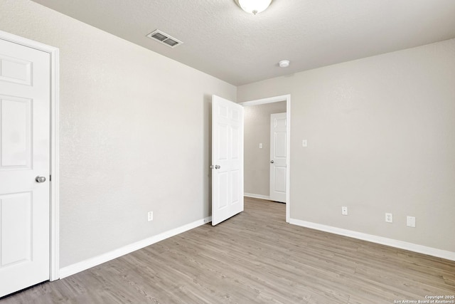 empty room featuring light wood finished floors, baseboards, visible vents, and a textured ceiling