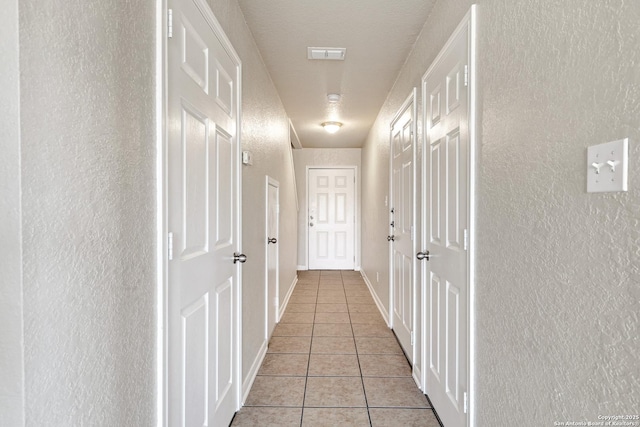 hallway with light tile patterned floors, baseboards, visible vents, and a textured wall