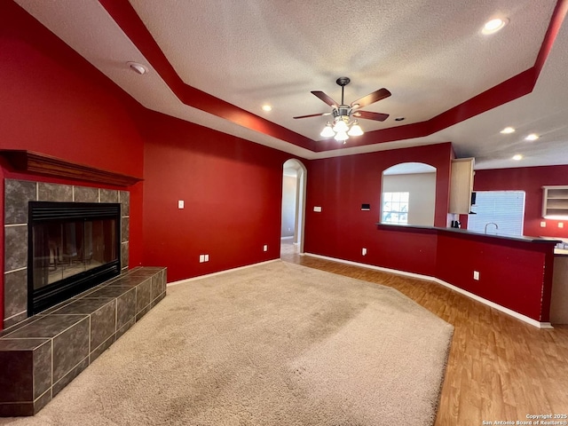 unfurnished living room featuring baseboards, arched walkways, a raised ceiling, a tiled fireplace, and a textured ceiling