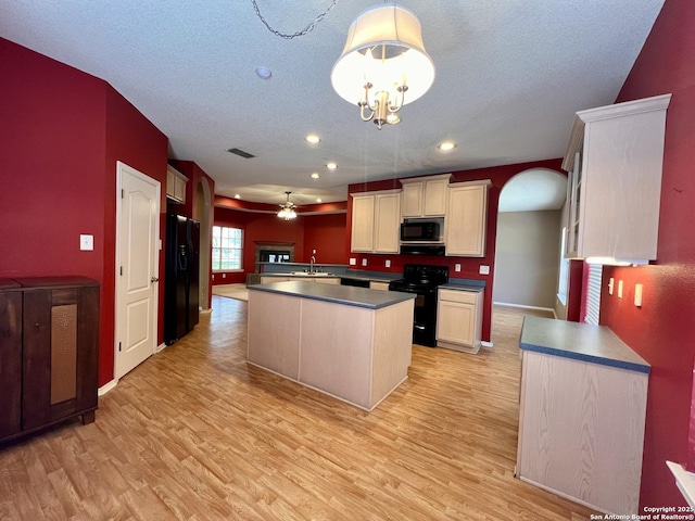 kitchen with arched walkways, dark countertops, a center island, light wood-type flooring, and black appliances