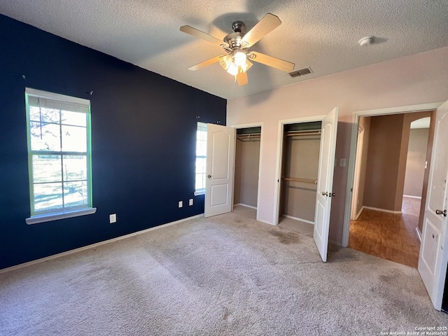 unfurnished bedroom featuring multiple windows, visible vents, multiple closets, and light colored carpet