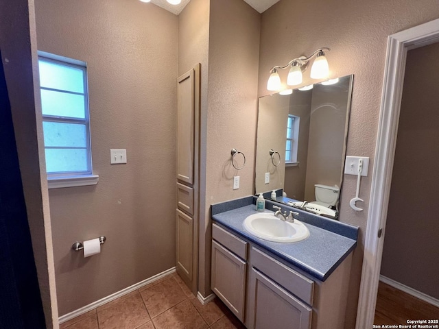 half bath with toilet, tile patterned flooring, vanity, and baseboards