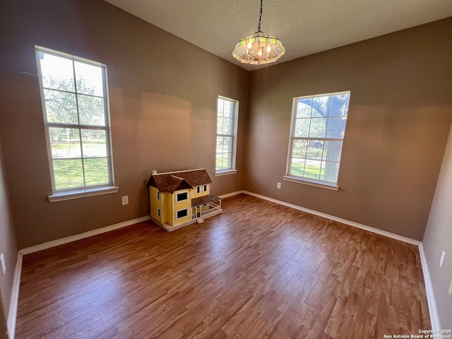 spare room with a healthy amount of sunlight, an inviting chandelier, baseboards, and wood finished floors