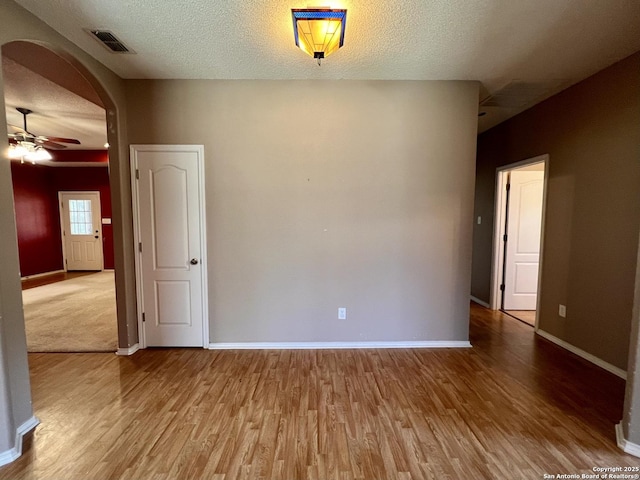 spare room featuring arched walkways, visible vents, ceiling fan, wood finished floors, and baseboards