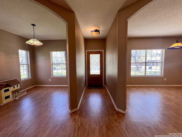 entryway with arched walkways, a textured ceiling, a chandelier, dark wood-type flooring, and baseboards