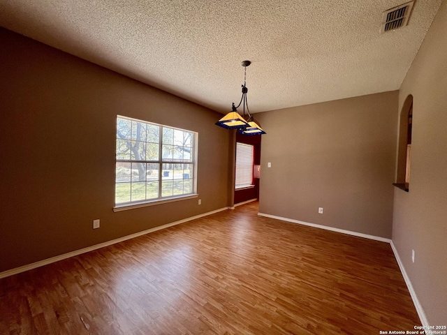 unfurnished room featuring visible vents, a textured ceiling, baseboards, and wood finished floors