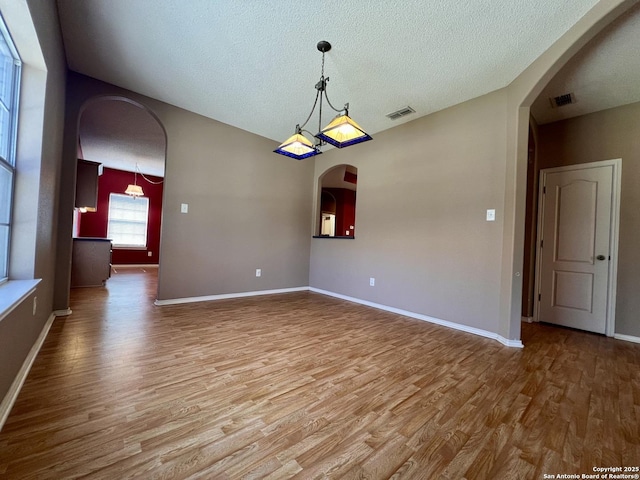 empty room featuring arched walkways, visible vents, baseboards, and wood finished floors