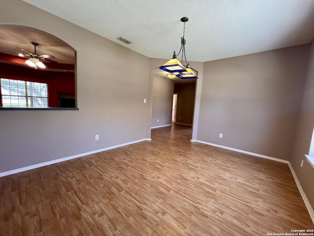 unfurnished room featuring arched walkways, visible vents, a ceiling fan, wood finished floors, and baseboards