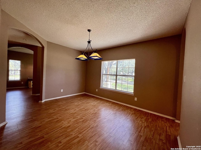 spare room featuring arched walkways, a textured ceiling, baseboards, and wood finished floors