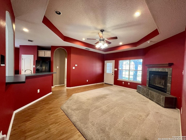 unfurnished living room featuring a tray ceiling, a fireplace, arched walkways, and baseboards