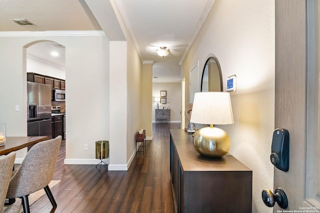 corridor featuring arched walkways, dark wood finished floors, visible vents, ornamental molding, and baseboards