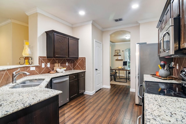 kitchen with arched walkways, dark wood-style flooring, stainless steel appliances, a sink, and dark brown cabinetry