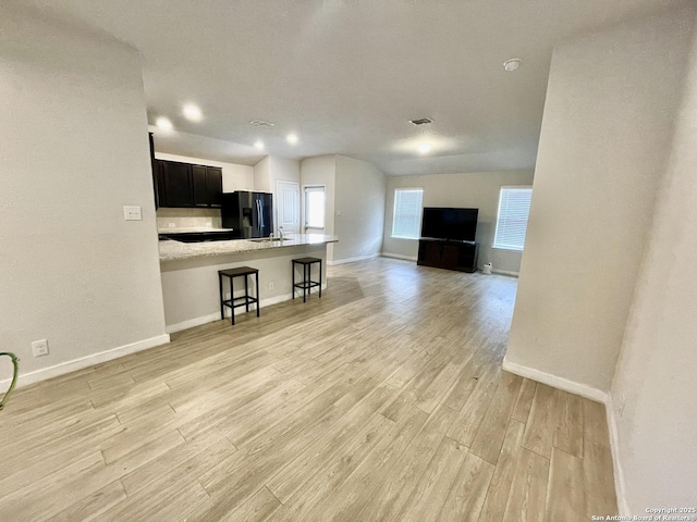 kitchen with a kitchen bar, light wood-style flooring, open floor plan, fridge with ice dispenser, and baseboards