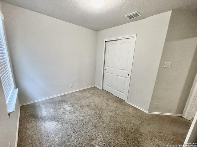 unfurnished bedroom with baseboards, visible vents, a textured ceiling, carpet flooring, and a closet