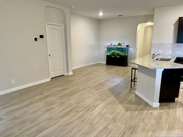 kitchen featuring arched walkways, light stone countertops, light wood-type flooring, a kitchen bar, and a sink