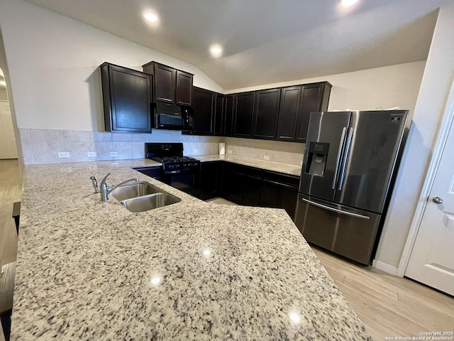 kitchen featuring light wood-style floors, vaulted ceiling, a sink, light stone countertops, and black appliances