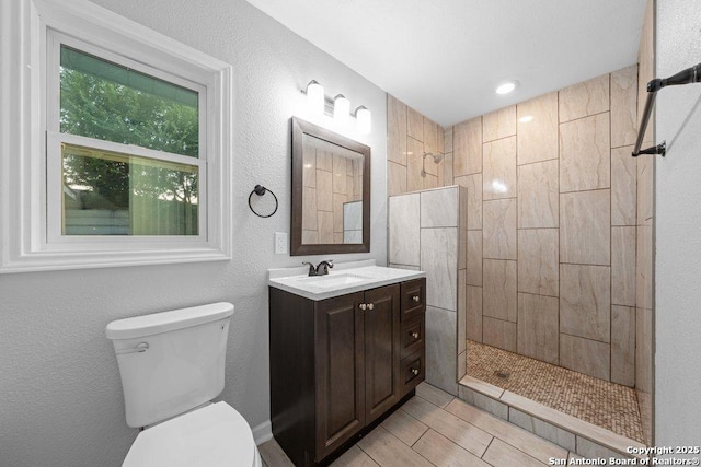 bathroom with tiled shower, a textured wall, vanity, and toilet