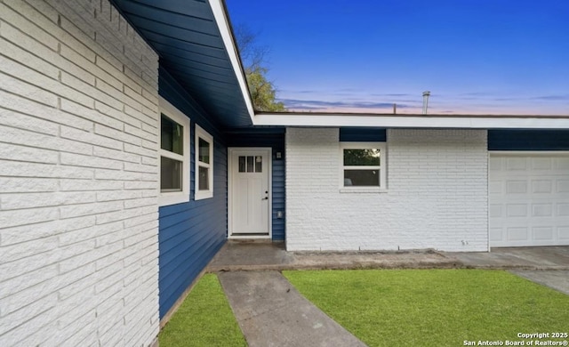 exterior entry at dusk with a garage and brick siding