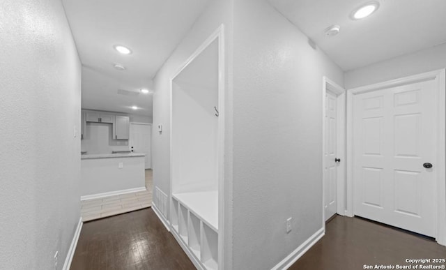 hall with a textured wall, baseboards, dark wood finished floors, and recessed lighting