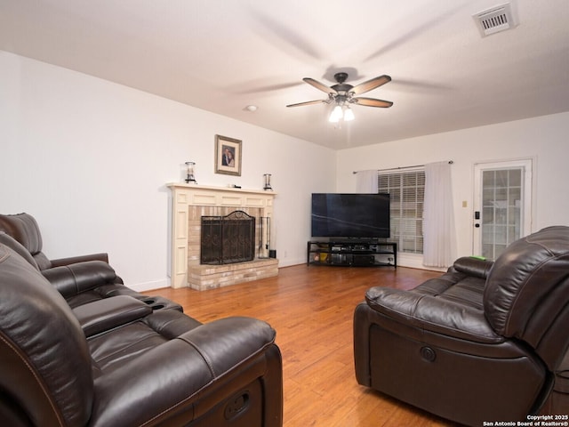 living room featuring baseboards, visible vents, ceiling fan, wood finished floors, and a fireplace