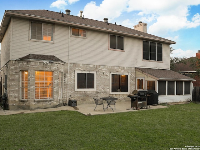 rear view of property featuring a yard, a chimney, brick siding, and a patio