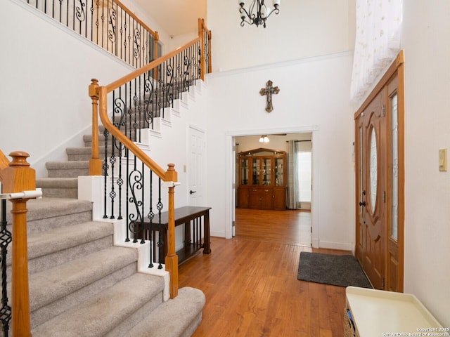 entryway with hardwood / wood-style flooring, a high ceiling, a chandelier, baseboards, and stairs