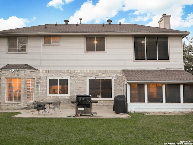 back of house featuring a patio area, a chimney, brick siding, and a yard