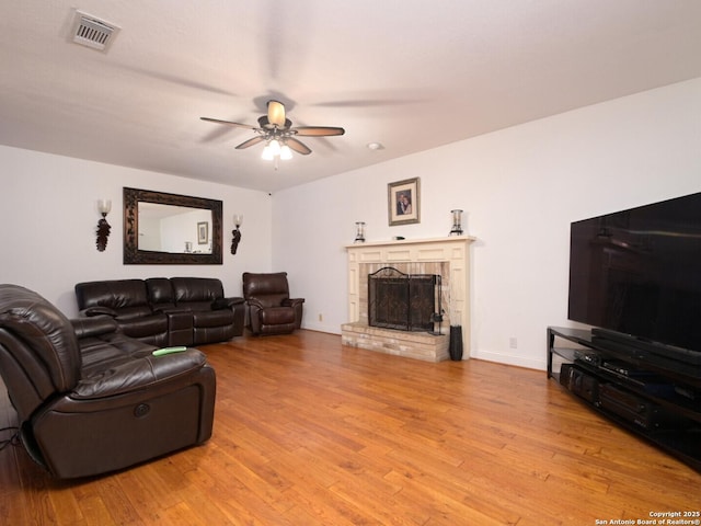 living area with a fireplace with raised hearth, visible vents, baseboards, a ceiling fan, and light wood-type flooring