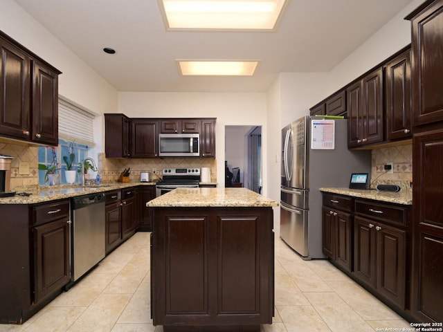 kitchen featuring light stone counters, decorative backsplash, appliances with stainless steel finishes, a kitchen island, and dark brown cabinets