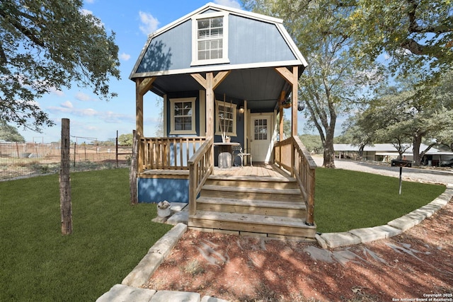 view of front of house with a front yard, covered porch, fence, and a gambrel roof