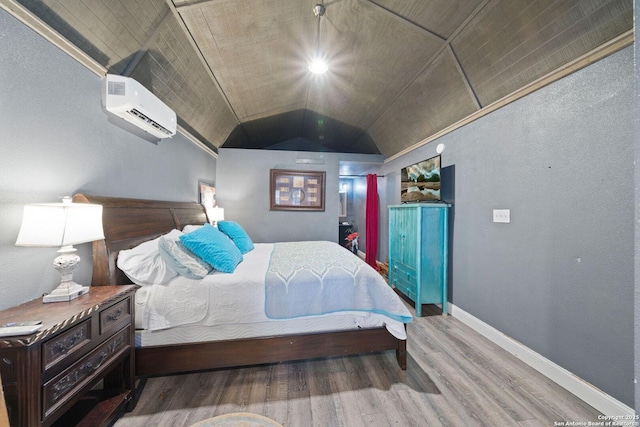 bedroom with an AC wall unit, vaulted ceiling, baseboards, and wood finished floors