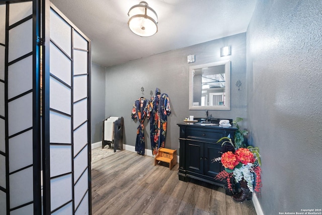 hall featuring a textured wall, baseboards, and wood finished floors