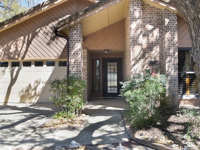 doorway to property featuring a garage, aphalt driveway, and brick siding