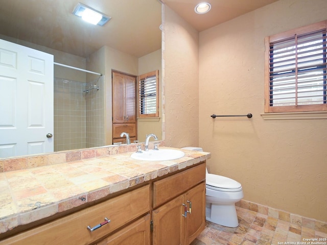 bathroom featuring a textured wall, toilet, vanity, tiled shower, and baseboards