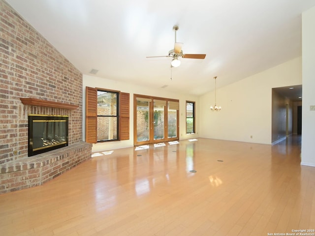 unfurnished living room with high vaulted ceiling, ceiling fan with notable chandelier, a fireplace, and wood finished floors