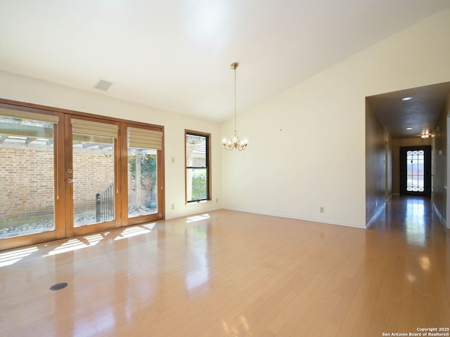 unfurnished room with lofted ceiling, a notable chandelier, a wealth of natural light, and wood finished floors