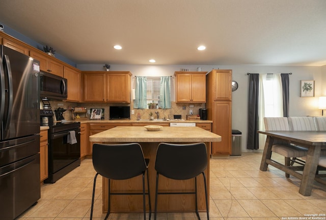 kitchen with light tile patterned floors, light countertops, a center island, black appliances, and tasteful backsplash