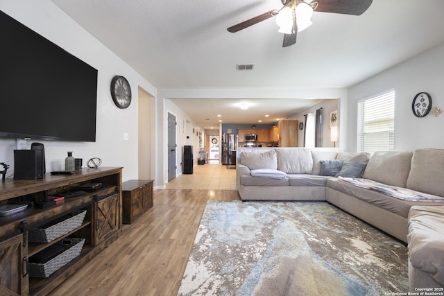 living room with light wood-style floors, ceiling fan, and visible vents