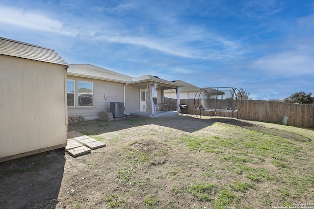 view of yard featuring a trampoline, fence, and central air condition unit