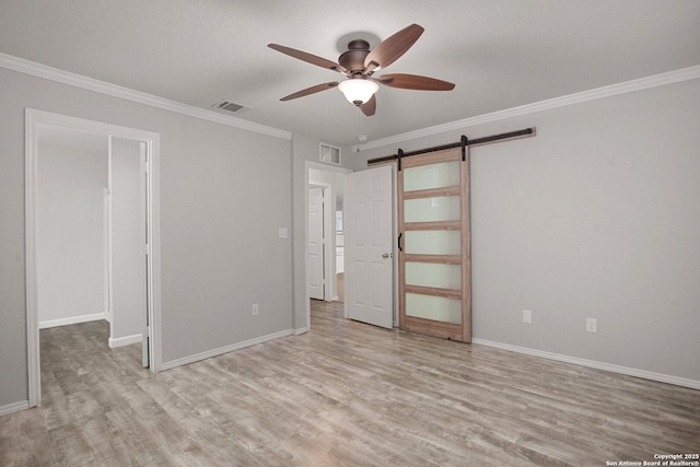 unfurnished bedroom featuring a barn door, crown molding, visible vents, and wood finished floors