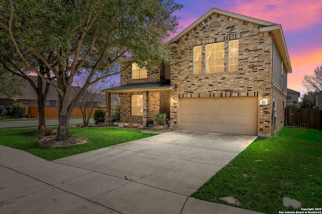 traditional-style house featuring fence, a yard, an attached garage, concrete driveway, and brick siding