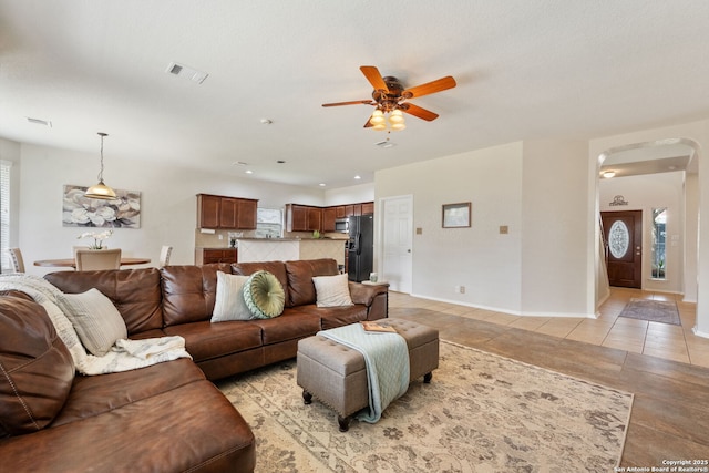 living room featuring visible vents, a ceiling fan, arched walkways, light tile patterned flooring, and baseboards