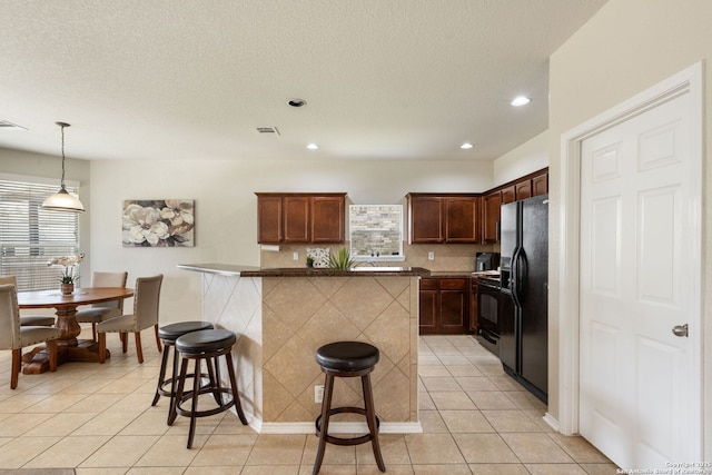 kitchen featuring visible vents, black appliances, a kitchen breakfast bar, tasteful backsplash, and light tile patterned floors