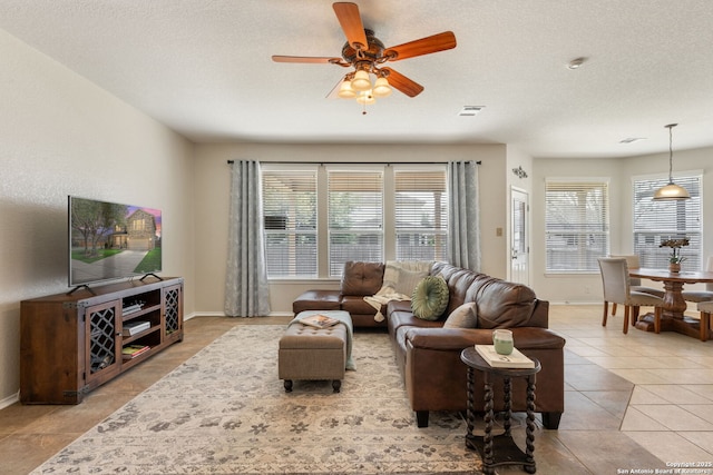 living room featuring light tile patterned flooring, a textured ceiling, baseboards, and a ceiling fan