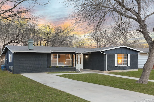 view of front of home featuring a chimney, a front lawn, concrete driveway, and brick siding